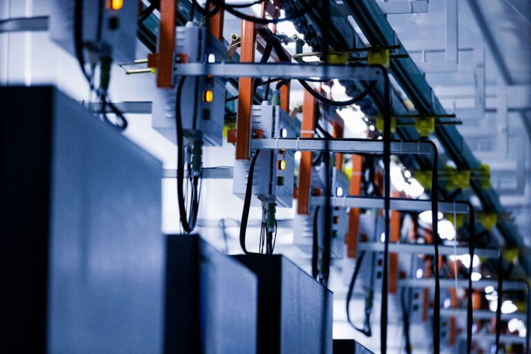 Rows of gray control boxes with illuminated indicators and black cables mounted on orange frames above industrial equipment.
